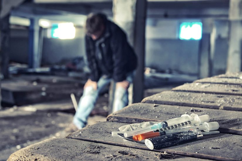 A youth getting a dose of a drug in an abandoned warehouse